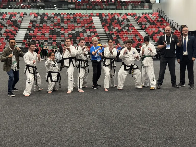 Inclusive Taekwon-Do athletes in fighting stances beside event officials in a large arena
