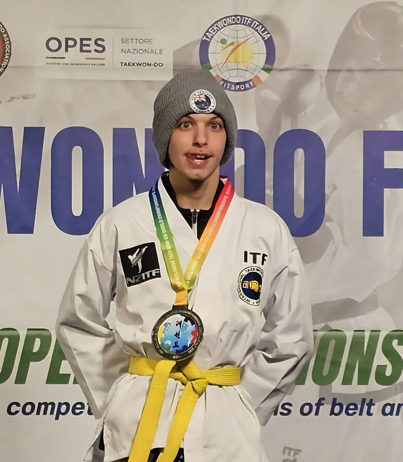 A yellow belt athlete in a beanie proudly wearing his medal in Italy